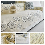 Une housse de canapé douce et décorative avec des motifs de fleurs blanches et noires sur un fond beige rayé, complétée par un coussin orné et un élément en peluche, pour un bel ensemble de chambre ou de salon.