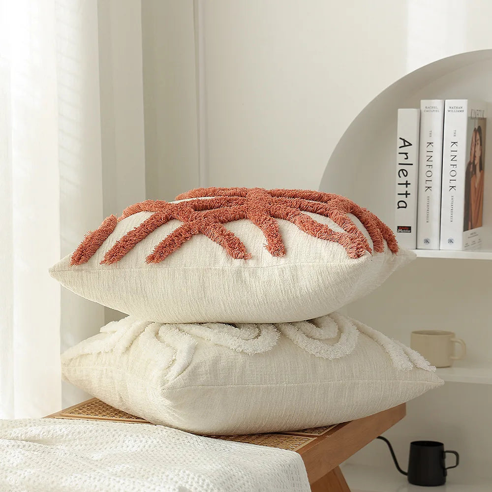Coussin décoratif avec des motifs floraux en relief dans des tons de rouille posé sur une pile de coussins blancs, avec des livres alignés en arrière-plan.