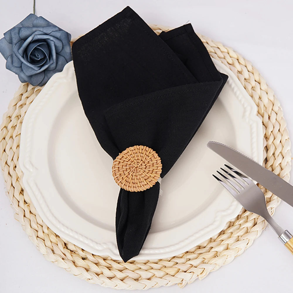 Élégante assiette blanche avec serviette de table noire, napperon tressé beige et décoration florale.