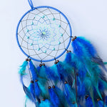 Un capteur de rêves bleu avec un motif en forme d'étoile et des plumes bleues et vertes, suspendu sur un fond blanc.