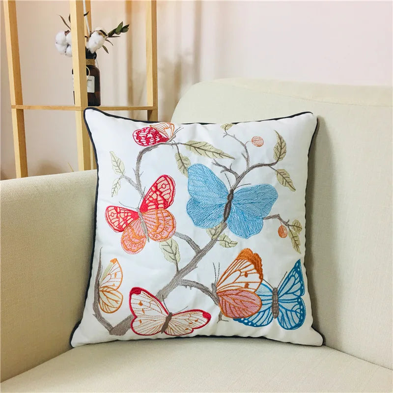 Coussin décoratif orné de papillons multicolores brodés sur un fond blanc, créant une atmosphère douce et apaisante.