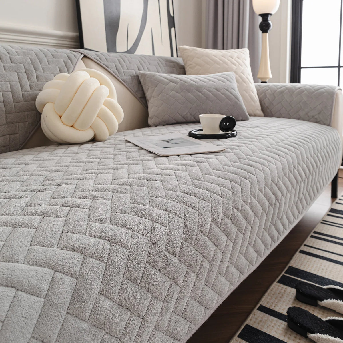 Chambre cocooning avec un canapé gris matelassé, une lampe de chevet élégante et des coussins moelleux créant une atmosphère apaisante et confortable.