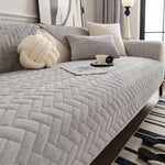 Chambre cocooning avec un canapé gris matelassé, une lampe de chevet élégante et des coussins moelleux créant une atmosphère apaisante et confortable.