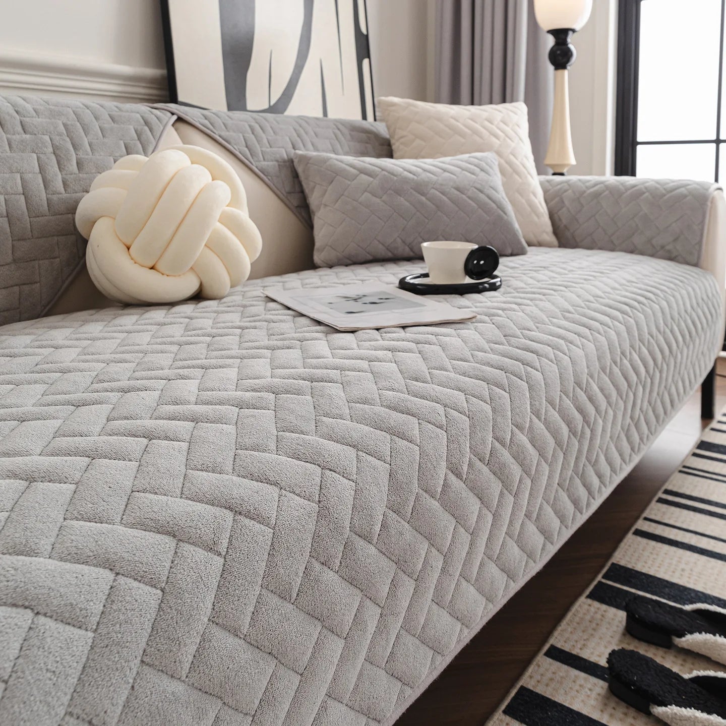 Chambre cocooning avec un canapé gris matelassé, une lampe de chevet élégante et des coussins moelleux créant une atmosphère apaisante et confortable.