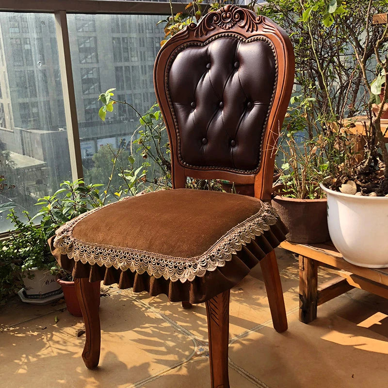 Chaise ancienne en bois sculpté, avec un dossier capitonné en cuir marron et un siège orné de dentelle, placée dans un environnement verdoyant avec des plantes en pot.