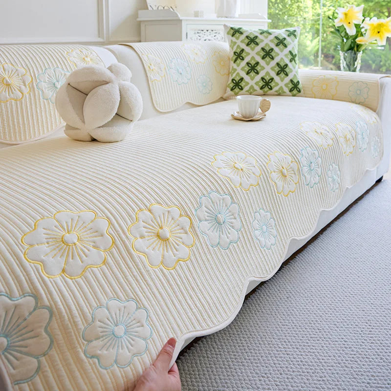 Un couvre-lit blanc et fleuri décoré de motifs de fleurs jaunes et bleues sur un canapé confortable dans un intérieur lumineux avec des touches de vert.