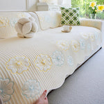 Un couvre-lit blanc et fleuri décoré de motifs de fleurs jaunes et bleues sur un canapé confortable dans un intérieur lumineux avec des touches de vert.