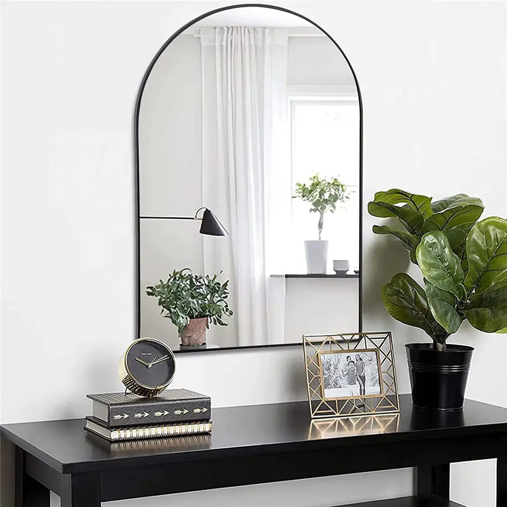 Élégante console noire avec grand miroir arqué, décorée de plantes vertes, de livres et d'un cadre photo.