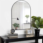 Élégante console noire avec grand miroir arqué, décorée de plantes vertes, de livres et d'un cadre photo.