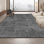 Un tapis gris foncé recouvre le sol d'un salon spacieux avec de grandes fenêtres offrant une vue sur un paysage forestier enneigé.