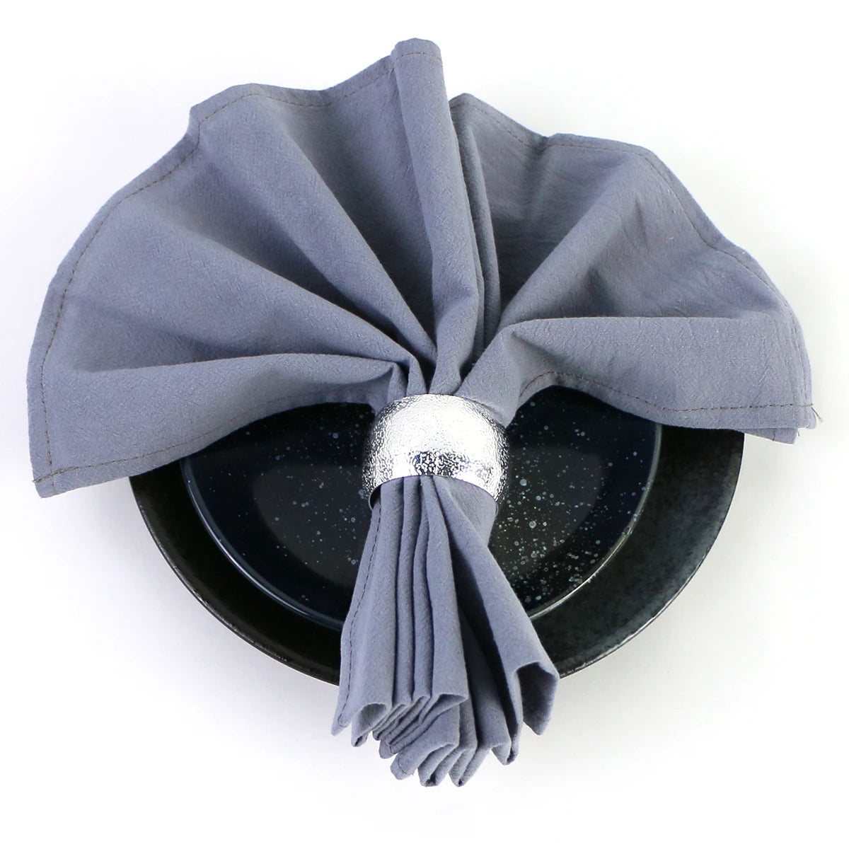 Une nappe de table de couleur grise foncée, avec des plis et une boucle décorative en argent, sur un fond sombre.