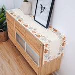 Meuble en bois clair avec un motif floral automnal sur le devant, posé sur un sol en parquet et décoré d'un cadre et d'un vase.