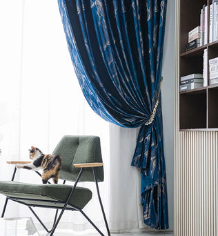 Chat sur un fauteuil vert à côté d’un rideau bleu foncé à motifs modernes dans un intérieur design