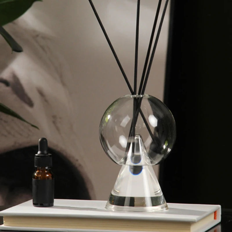 vase verre transparent diffuseur aromates socle triangulaire bâtonnets noirs plante pot blanc livres table