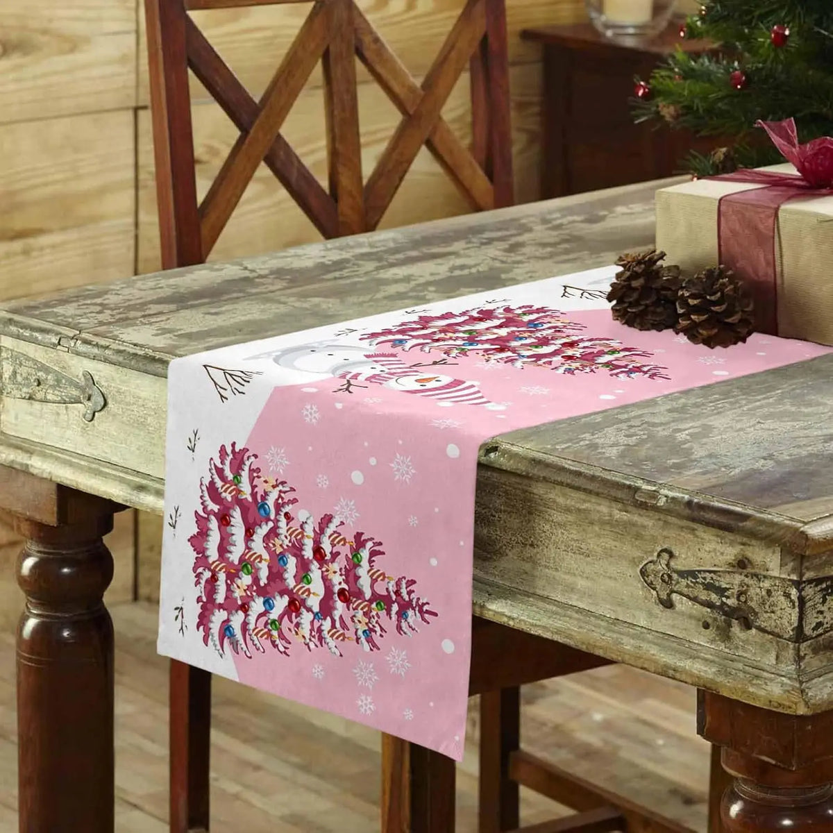 Ce chemin de table rose décoré de motifs d'arbres enneigés apporte une touche festive et hivernale à la décoration de la table.