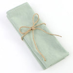 Élégante écharpe en tissu doux de couleur verte pâle, soigneusement enroulée et attachée par un joli lien de chanvre, créant une présentation raffinée et invitante.
