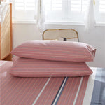 Des oreillers roses rayés, disposés sur un lit, dans une chambre aux tons clairs et apaisants.