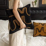 Coussin décoratif noir et jaune avec des motifs abstraits et graphiques, placé sur un lit.