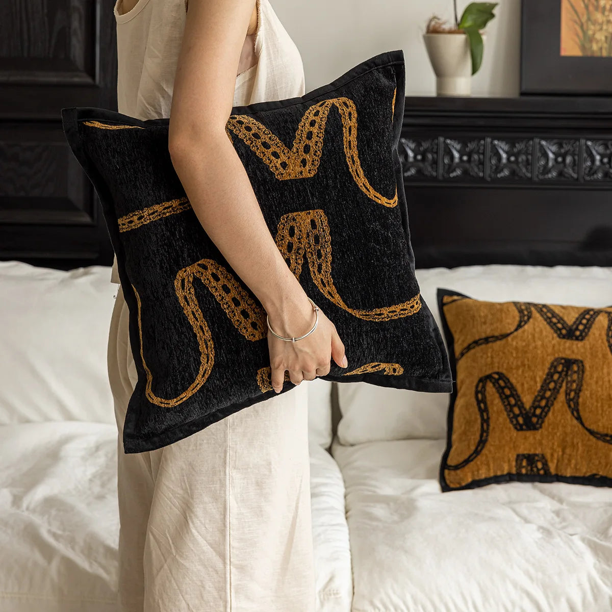 Coussin décoratif noir et jaune avec des motifs abstraits et graphiques, placé sur un lit.