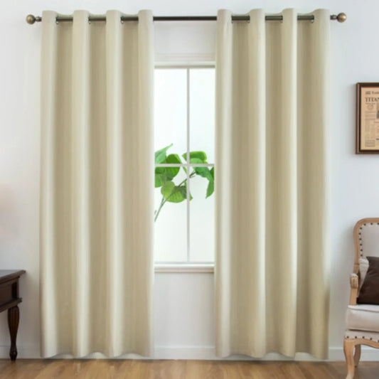 Paire de rideaux beiges unis installés sur une tringle noire dans un intérieur classique avec plante verte derrière la fenêtre et fauteuil beige à accoudoirs bois.