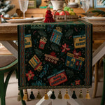 Nappe de table de Noël ornée de motifs festifs colorés et de franges décoratives, sur une table en bois avec des assiettes et des décorations de Noël.