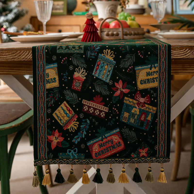 Nappe de table de Noël ornée de motifs festifs colorés et de franges décoratives, sur une table en bois avec des assiettes et des décorations de Noël.