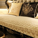 Un canapé élégant orné de décorations dorées, de coussins brodés et d'une couverture matelassée créant une atmosphère luxueuse.