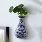 Un vase en céramique bleue et blanche décoré de motifs floraux ornementaux, rempli de feuilles vertes fraîches.