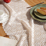 Un napperon blanc et élégant avec un motif géométrique décoratif, posé sur une table en bois avec des assiettes et des aliments.