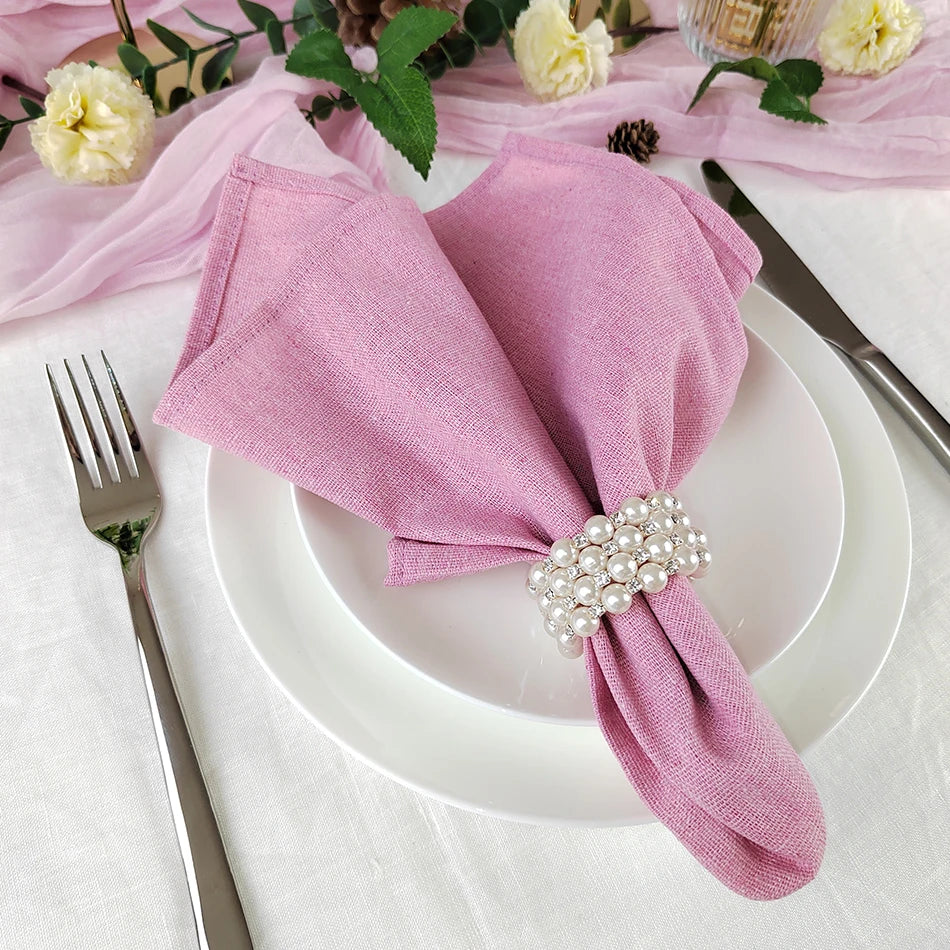 Une élégante serviette rose ornée d'une jolie broche de perles sur une assiette blanche avec couverts et fleurs d'automne, suggérant un élégant couvert de table.