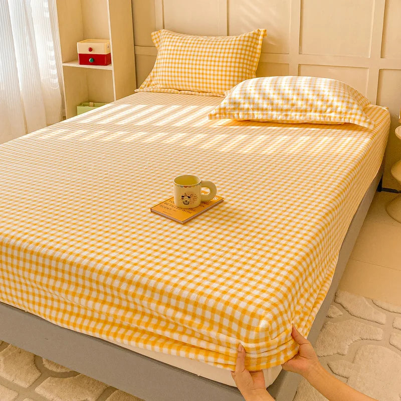 Une chambre confortable avec un couvre-lit jaune et blanc à carreaux, une tasse sur une petite table, créant une atmosphère chaleureuse et accueillante.