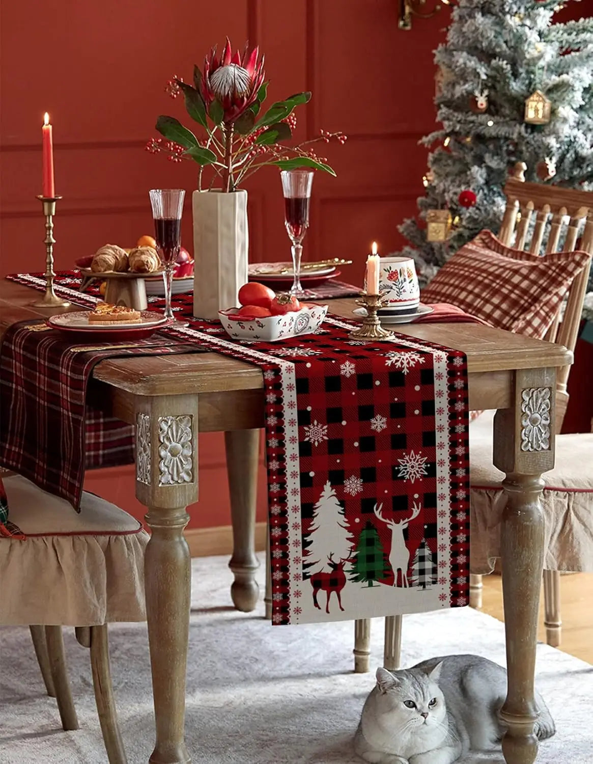 Intérieur douillet de Noël avec table dressée pour un repas, décorations festives, bougie allumée et chat gris sur le sol.