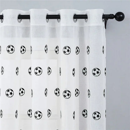 Voilage à œillets avec motifs de ballons de football, suspendu à une tringle noire sur un mur gris clair.