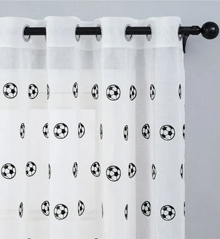 Voilage à œillets avec motifs de ballons de football, suspendu à une tringle noire sur un mur gris clair.