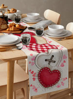 Une table joliment dressée avec des croissants, des plats et des verres de vin sur un chemin de table décoré de cœurs rouges et roses.