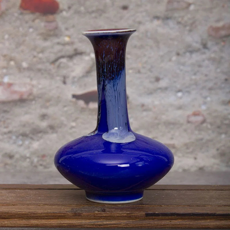 Vase en céramique bleu foncé avec un col effilé et une forme élégante, posé sur une surface en bois.