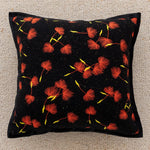 Coussin orné de fleurs rouges et jaunes sur fond noir, créant un motif floral vibrant et élégant.