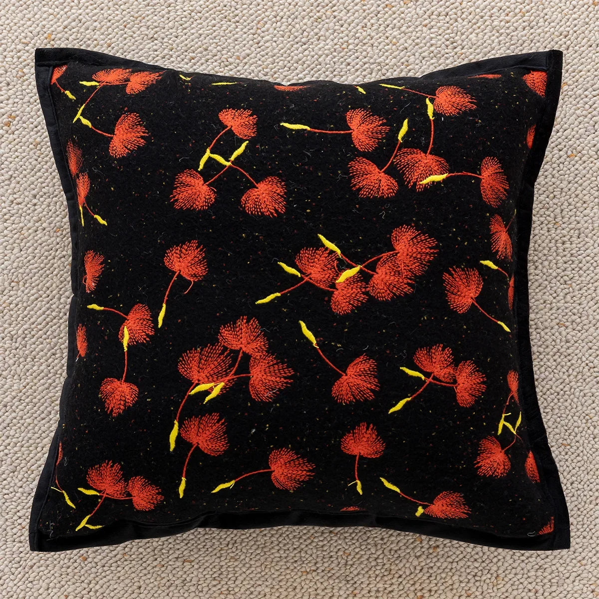 Coussin orné de fleurs rouges et jaunes sur fond noir, créant un motif floral vibrant et élégant.
