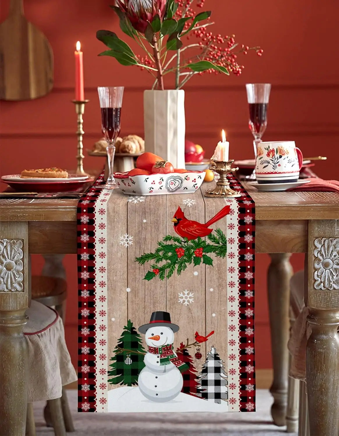 La table de fête est joliment décorée avec des fleurs de protée rouges, des bougies, des verres de vin et des plats de nourriture, ainsi qu'un chemin de table en bois peint avec un motif hivernal de flocons de neige et de bonhomme de neige.