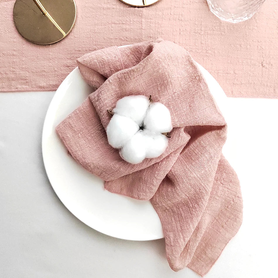 Composition harmonieuse avec une serviette de lin rose et des boules de coton disposées sur une assiette blanche, dans un décor élégant et minimaliste.