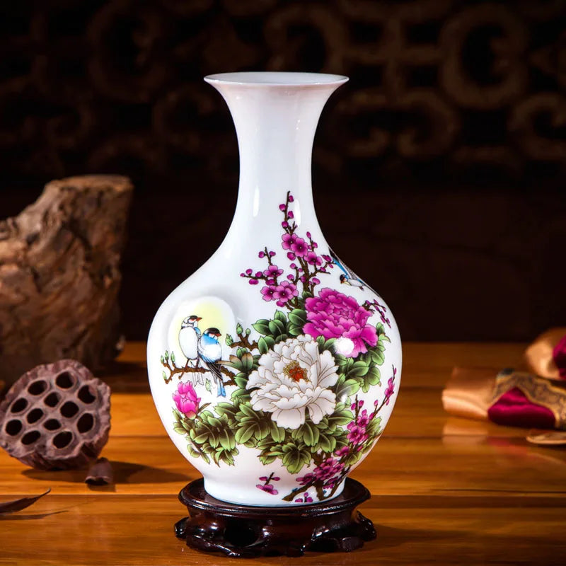 Un vase en céramique blanche décoré de fleurs roses, blanches et vertes sur un fond sombre, avec une monture en bois foncé.