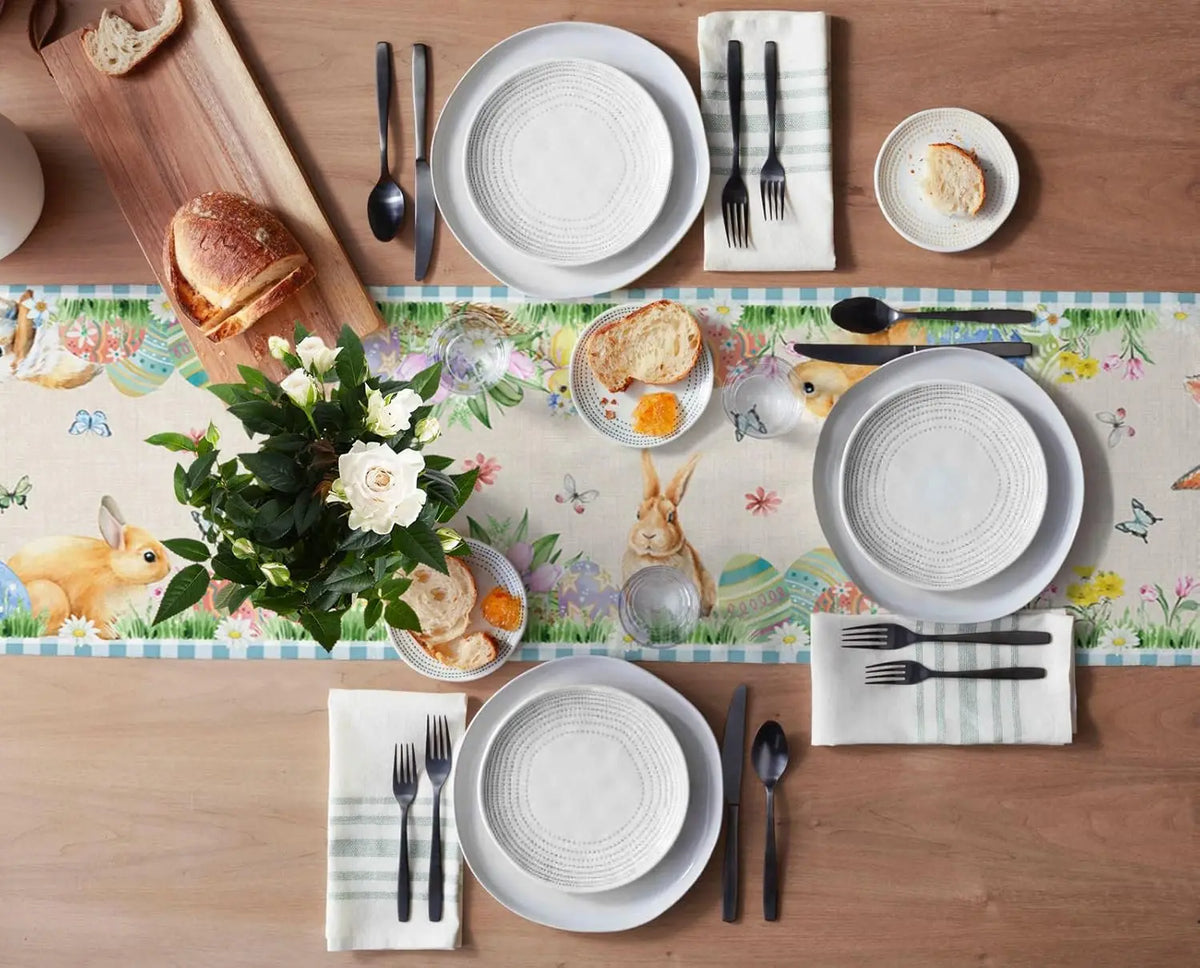 Table dressée avec des assiettes, couverts, serviettes et décorations florales sur un joli fond imprimé de motifs printaniers et d'animaux.