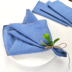 Serviettes de table bleues décorées d'une fleur verte, disposées sur une assiette blanche.