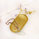 Plateau de service décoratif en métal doré avec branche florale, pendentif en perles et oiseau doré.