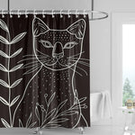 Rideau de douche noir avec un motif minimaliste de chat blanc entouré de fleurs, installé dans une salle de bain moderne avec une baignoire et une fenêtre lumineuse en arrière-plan.