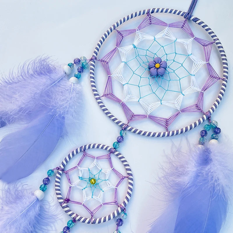 Attrape-rêves violet et bleu avec des perles et des plumes, suspendu sur un fond clair.
