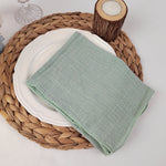 Sur une serviette en osier tressé, une assiette blanche est posée avec un linge de cuisine en lin vert menthe.