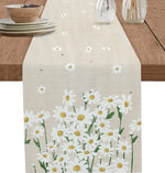 Table de cuisine avec un chemin de table décoré de motifs floraux blancs et jaunes de marguerites sur fond beige clair, donnant une ambiance printanière et naturelle.