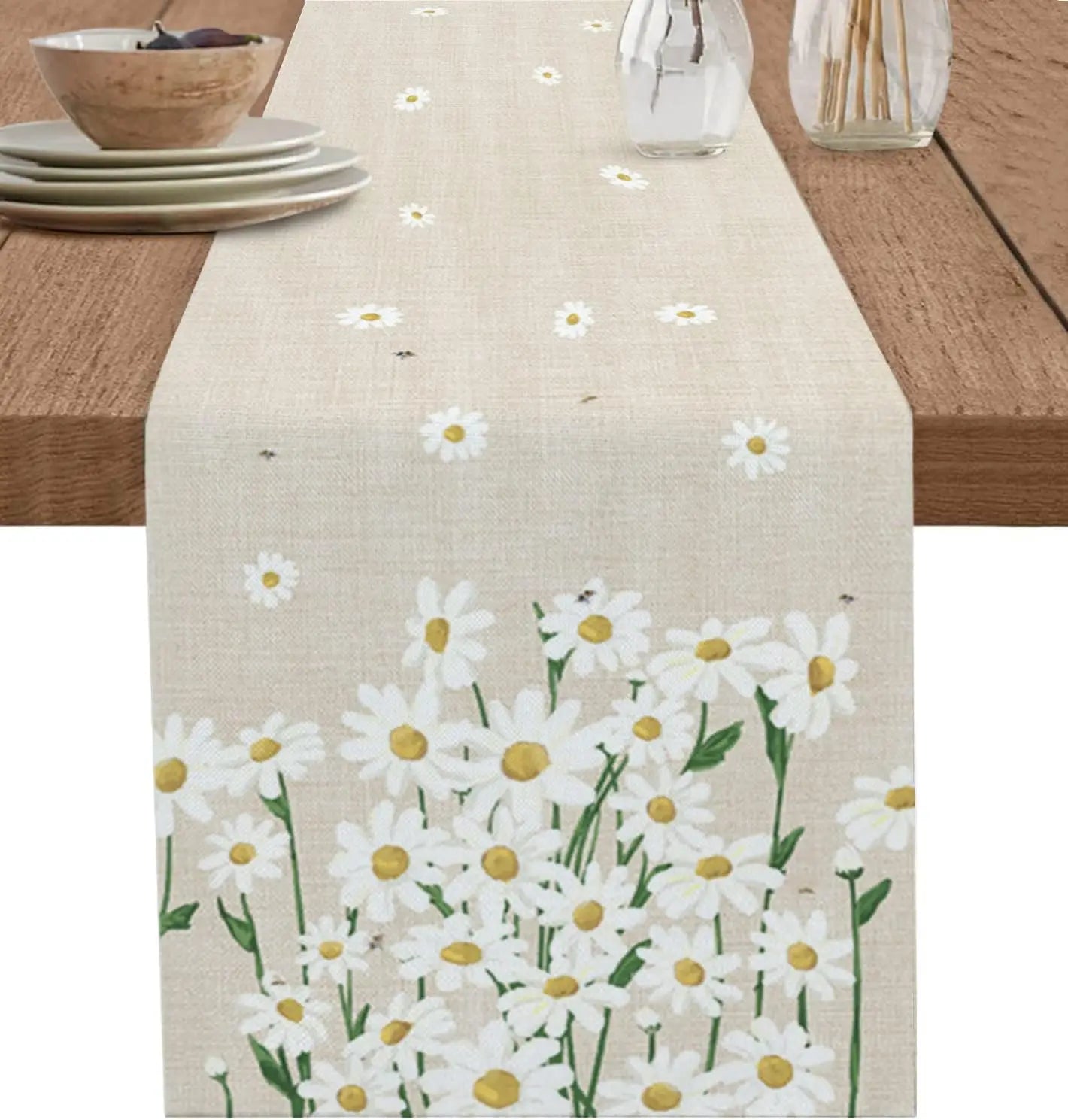 Table de cuisine avec un chemin de table décoré de motifs floraux blancs et jaunes de marguerites sur fond beige clair, donnant une ambiance printanière et naturelle.