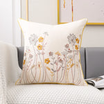 Coussin décoratif avec un motif floral élégant composé de fleurs et de feuillages brodés en couleurs chaudes sur un fond clair.